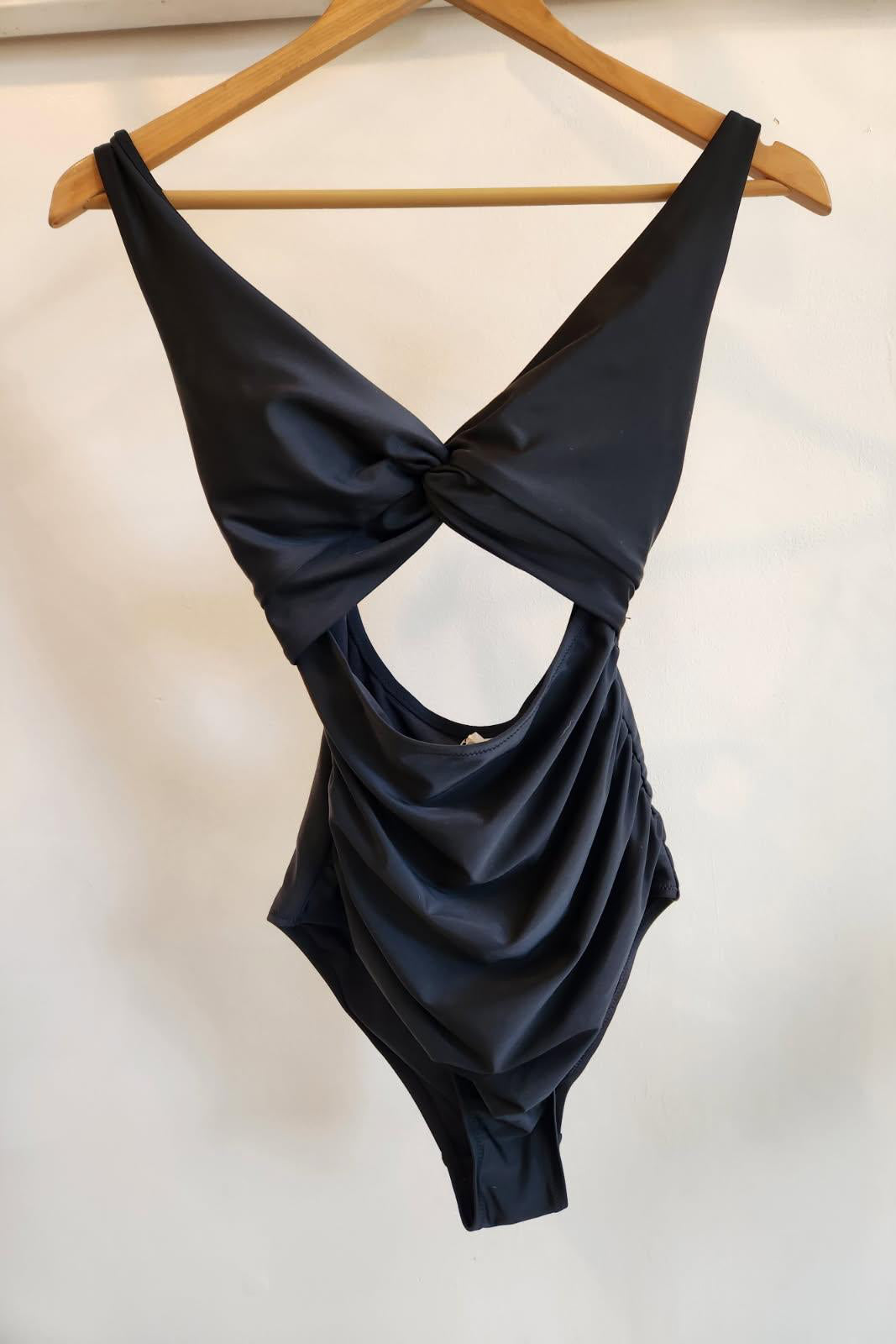 Black swimsuit on a wooden hanger against a white background
