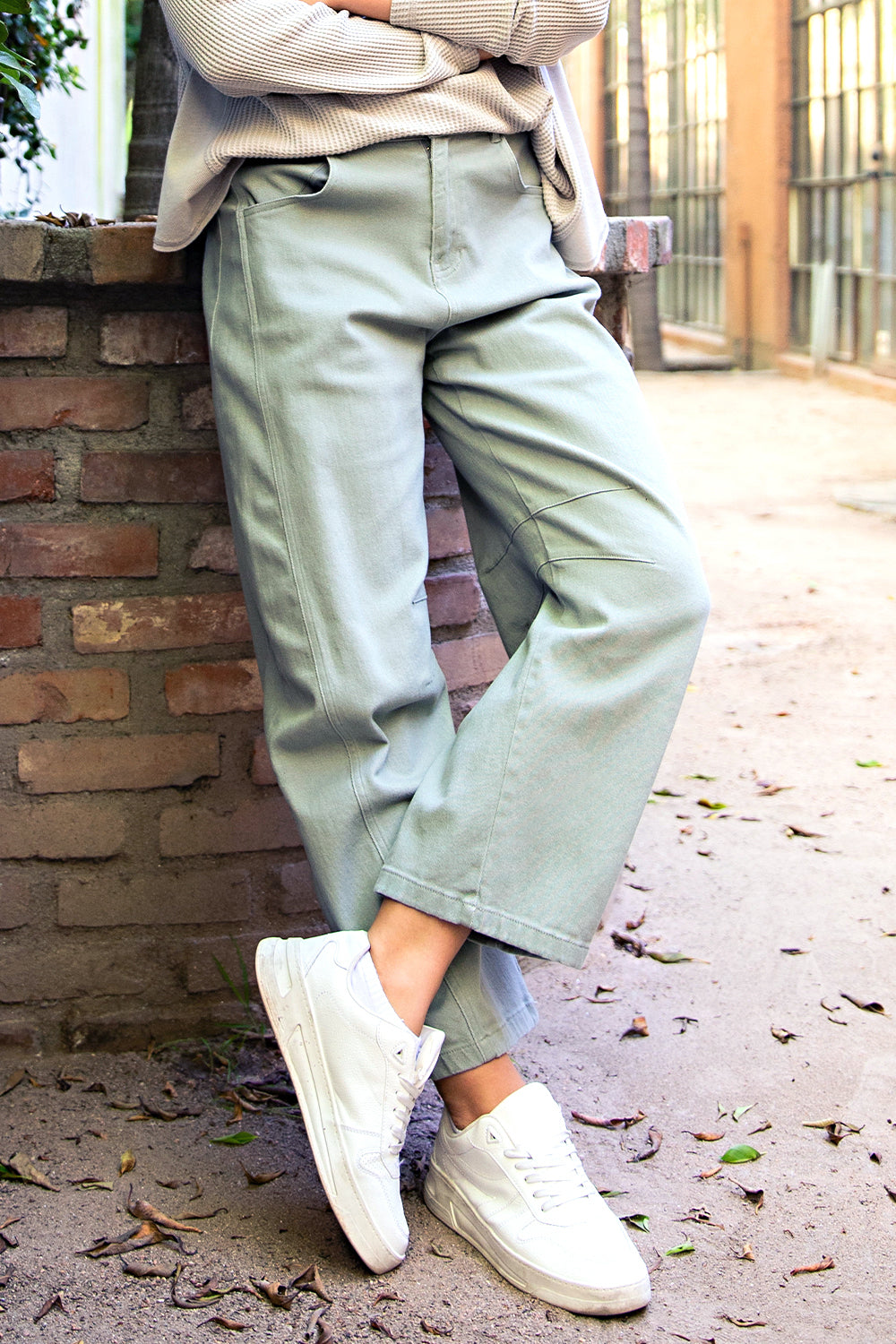 Person wearing light green pants and white sneakers leaning against a brick wall.