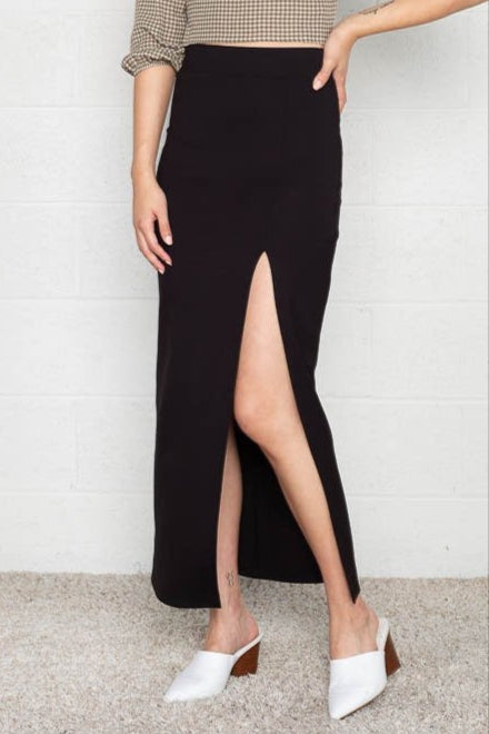 A person wearing a black maxi skirt with a slit, paired with a checkered shirt and white shoes.