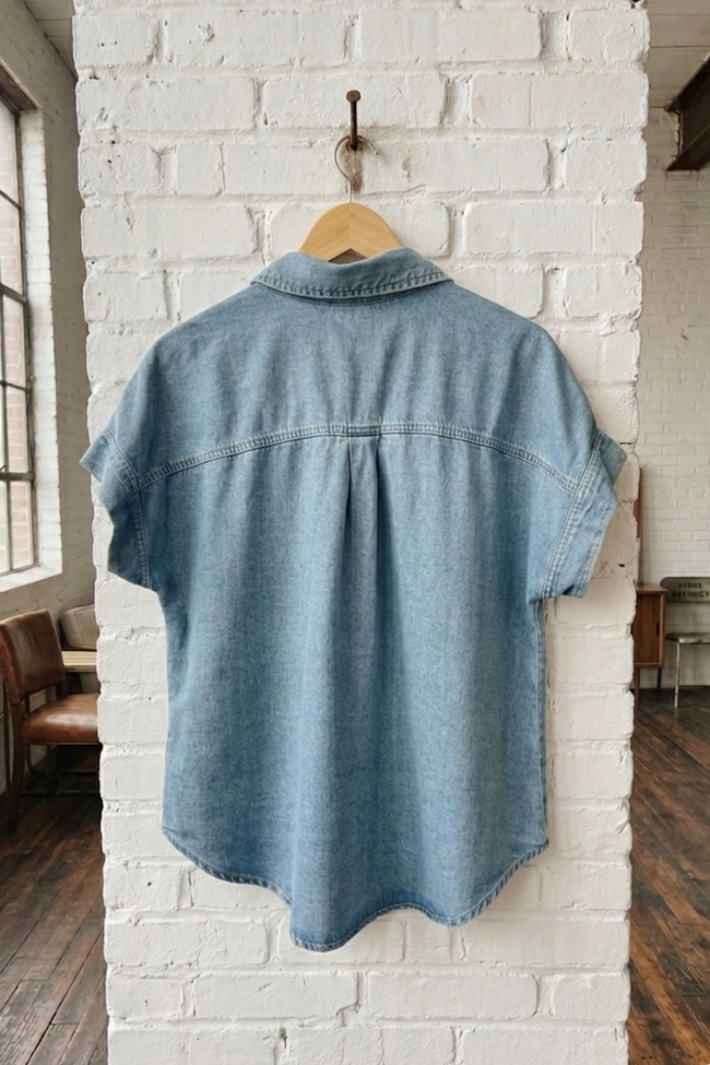 Blue denim shirt on a hanger against a white brick wall.