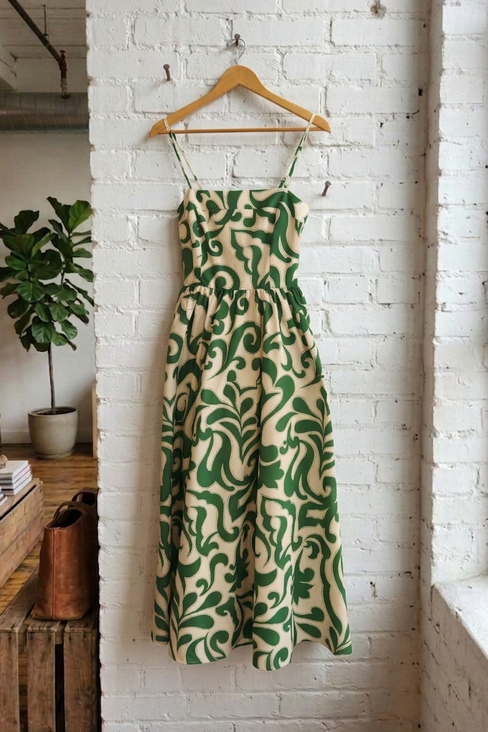 Green and beige patterned dress hanging on a wooden hanger against a white brick wall.
