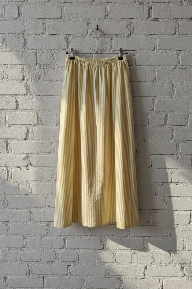 Yellow skirt hanging on a hook against a white brick wall.