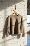 Brown sweater hanging on a hanger against a white brick wall.