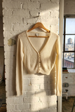 Beige cardigan hanging on a wooden hanger against a white brick wall with a cityscape view.