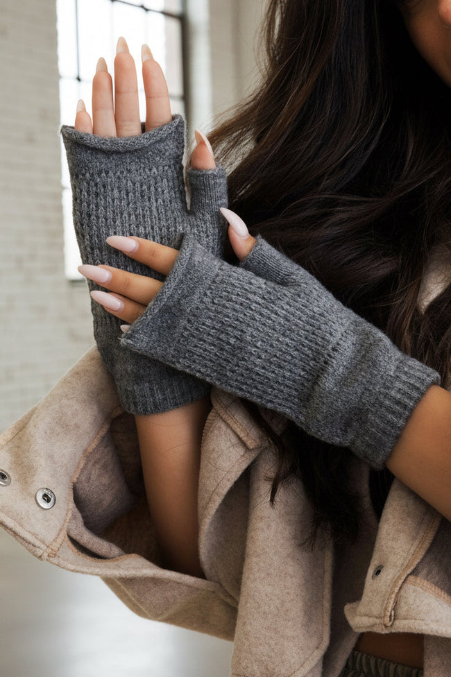 Person wearing gray knitted fingerless gloves against a beige background