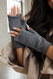 Person wearing gray knitted fingerless gloves against a beige background