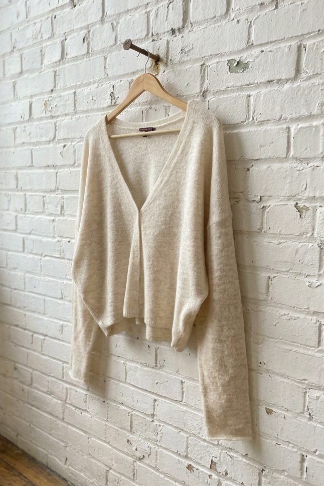 Beige sweater hanging on a wooden hanger against a white brick wall.