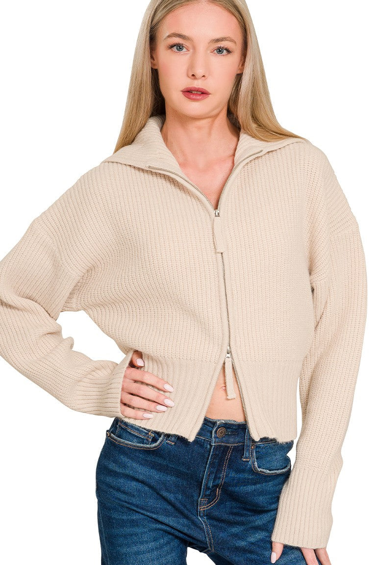 Woman wearing a beige zip-up sweater and blue jeans on a white background