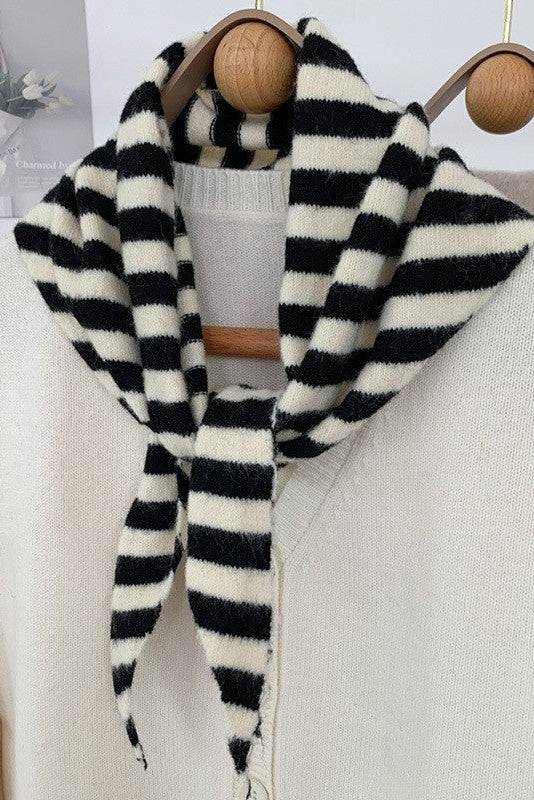 Black and white striped scarf draped over a beige sweater on a wooden hanger.
