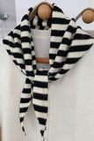 Black and white striped scarf draped over a beige sweater on a wooden hanger.