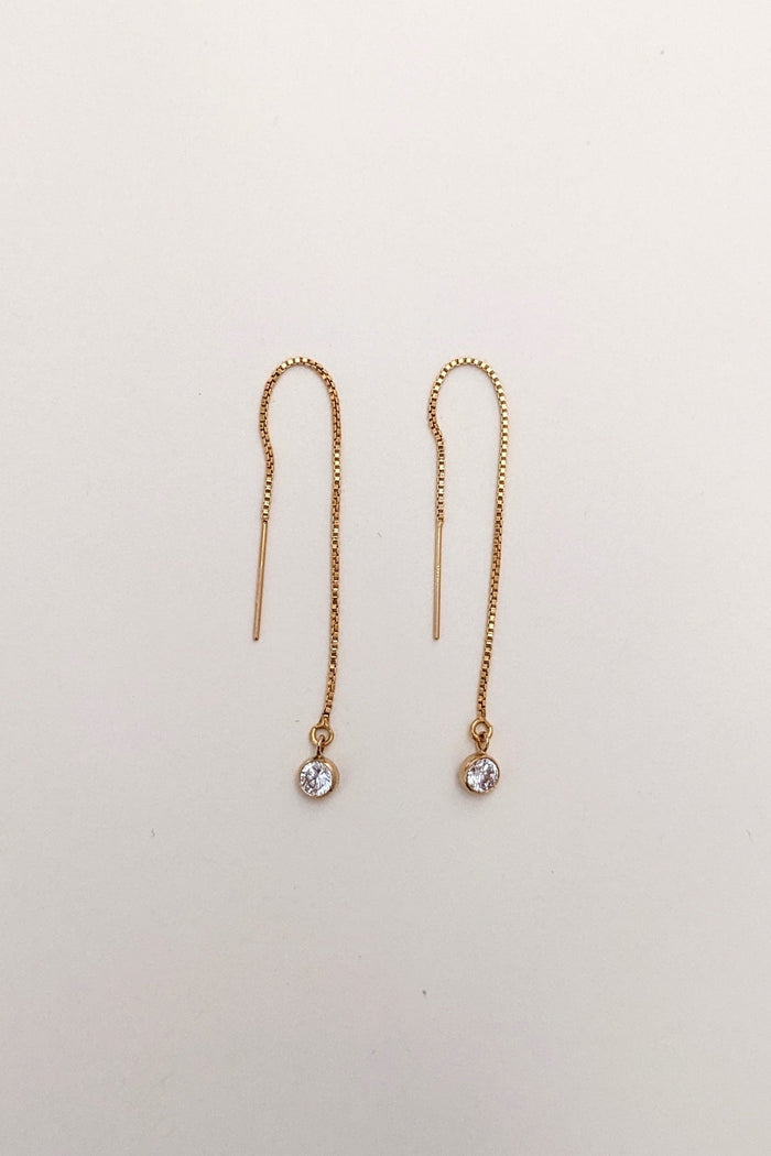 Pair of gold threader earrings with small gemstones on a light beige background