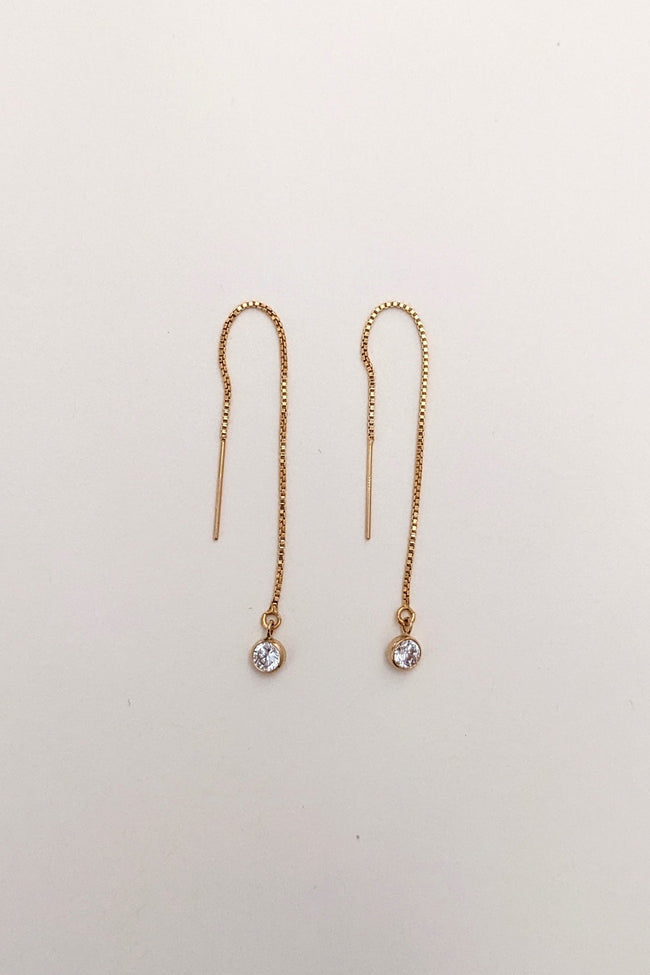 Pair of gold threader earrings with small gemstones on a light beige background