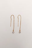 Pair of gold threader earrings with small gemstones on a light beige background
