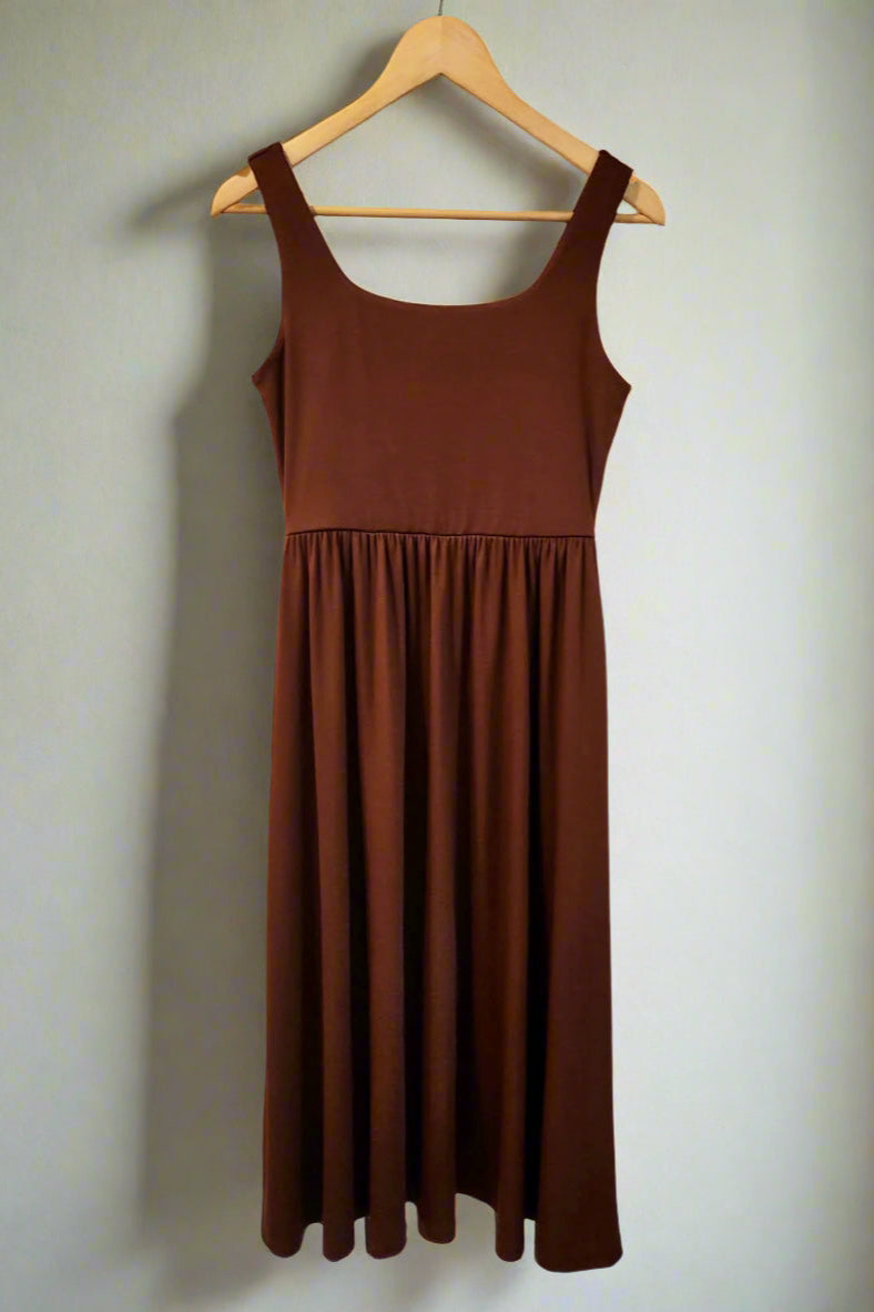 Brown dress hanging on a wooden hanger against a white wall.