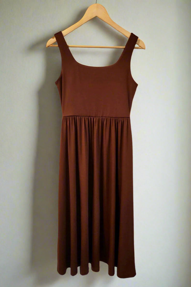 Brown dress hanging on a wooden hanger against a white wall.