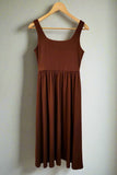 Brown dress hanging on a wooden hanger against a white wall.