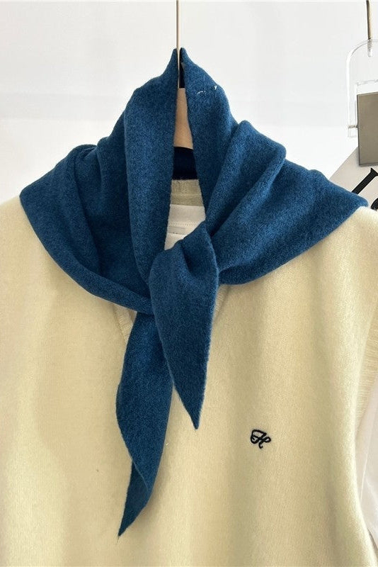 Blue scarf draped over a beige vest with a white background