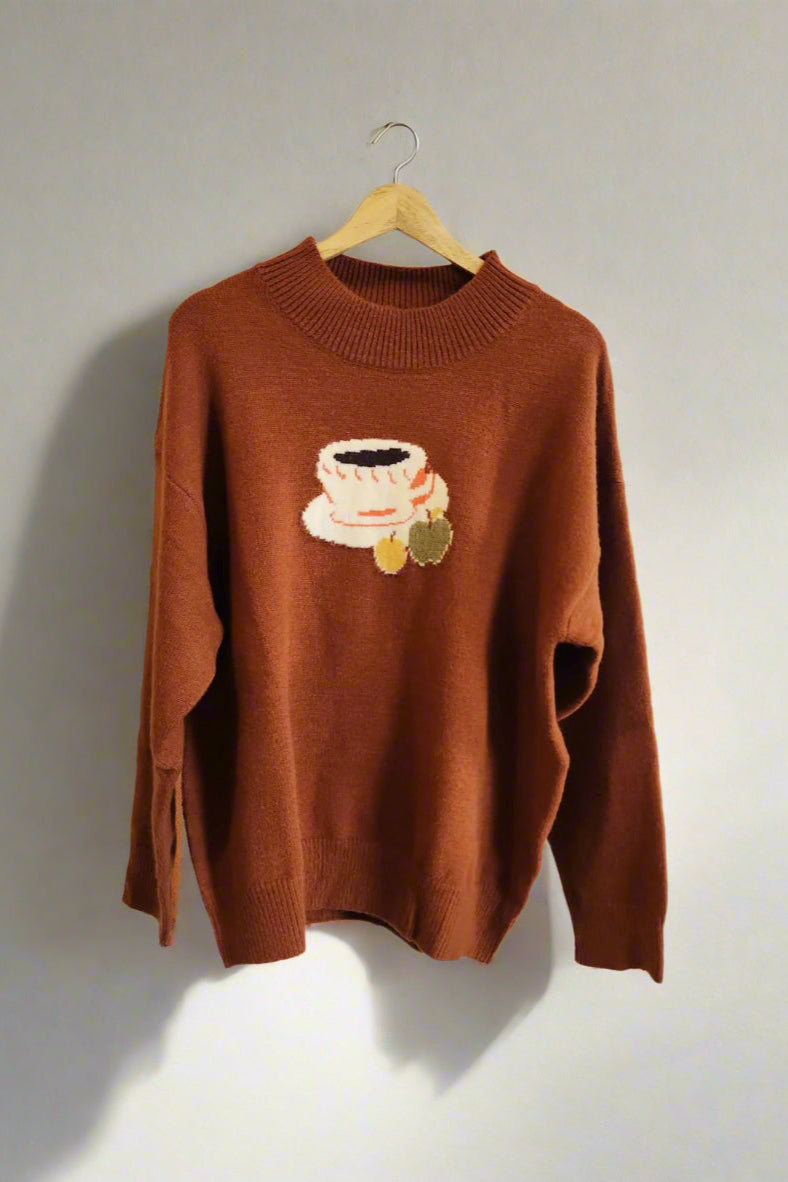 Brown sweater with a coffee cup design on a hanger against a white wall.