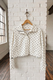 Polka dot jacket on a wooden hanger against a white brick wall.