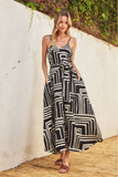 Woman wearing a black and white patterned dress standing against a white wall with greenery.