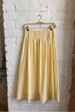 Yellow skirt hanging on a hanger against a white brick wall.