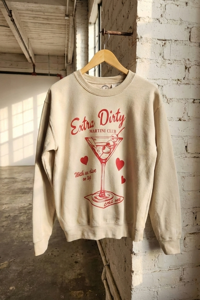 Beige sweatshirt with red graphic and text on a hanger against a brick wall.