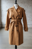 Brown trench coat on a mannequin against a brick wall.