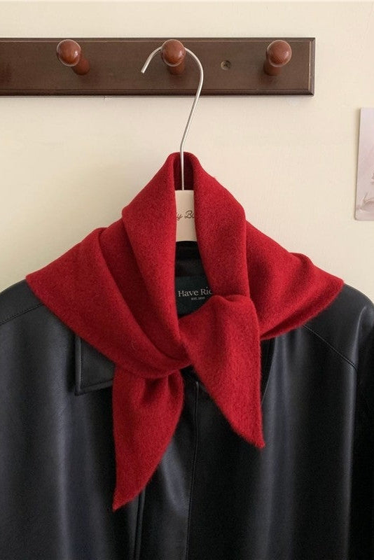 Red scarf draped over a black coat on a wooden hanger against a beige wall.