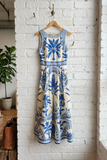 Blue and white floral dress hanging on a wooden hanger against a white brick wall.