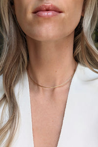 Close-up of a person wearing a delicate gold necklace with a blurred background