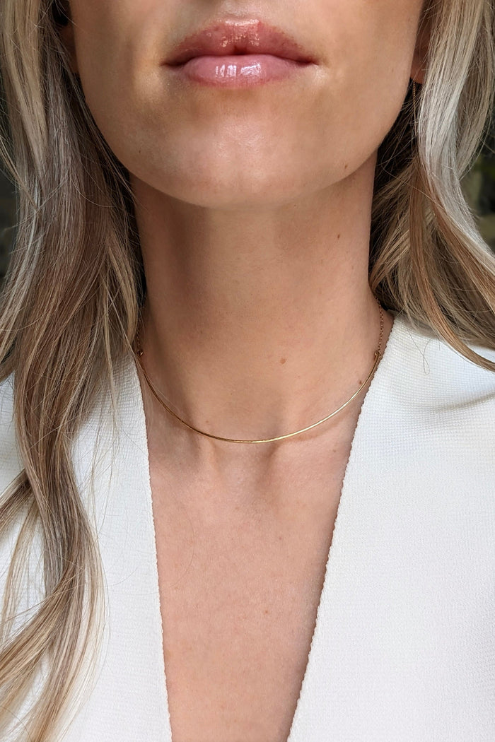 Close-up of a person wearing a delicate gold necklace with a blurred background
