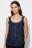 A woman wearing a navy blue sleeveless top with ruffled trim and a drawstring neckline, photographed against a light gray studio background.