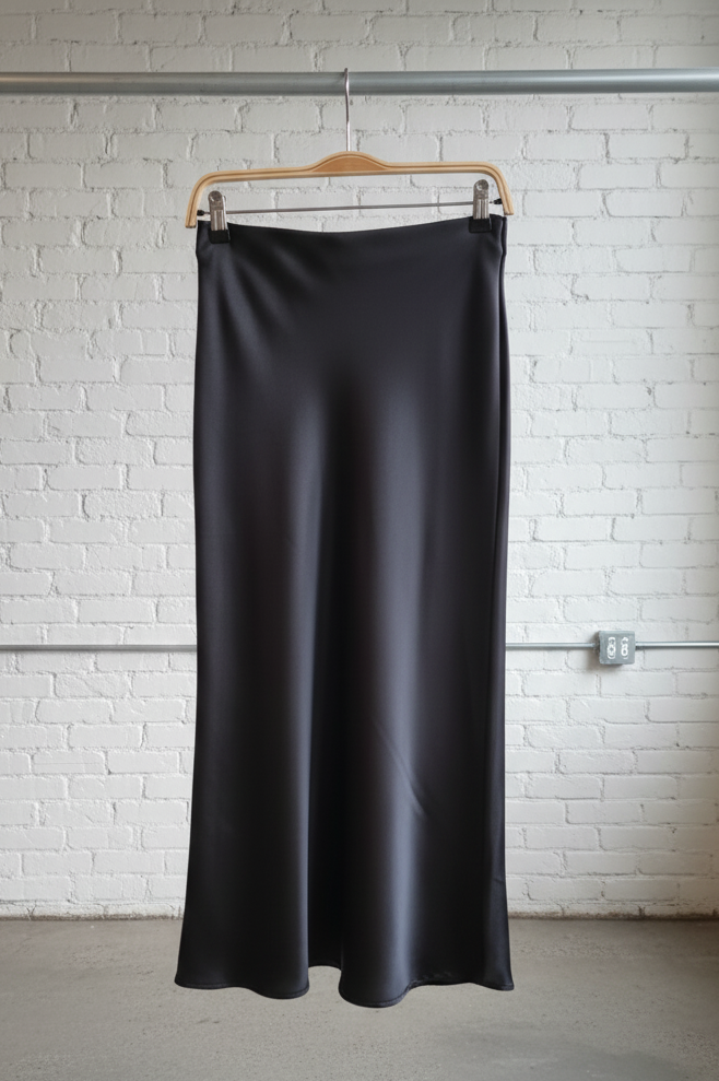 Black satin skirt on a hanger against a white brick wall.