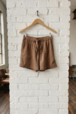 Brown shorts on a wooden hanger against a white brick wall.