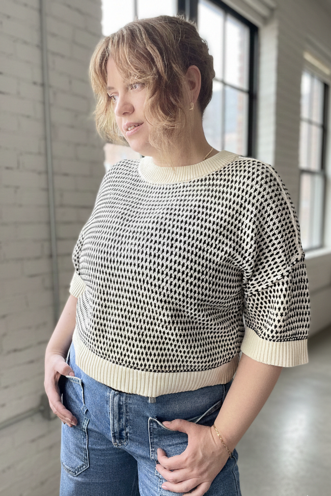Woman wearing a patterned sweater and jeans standing indoors.