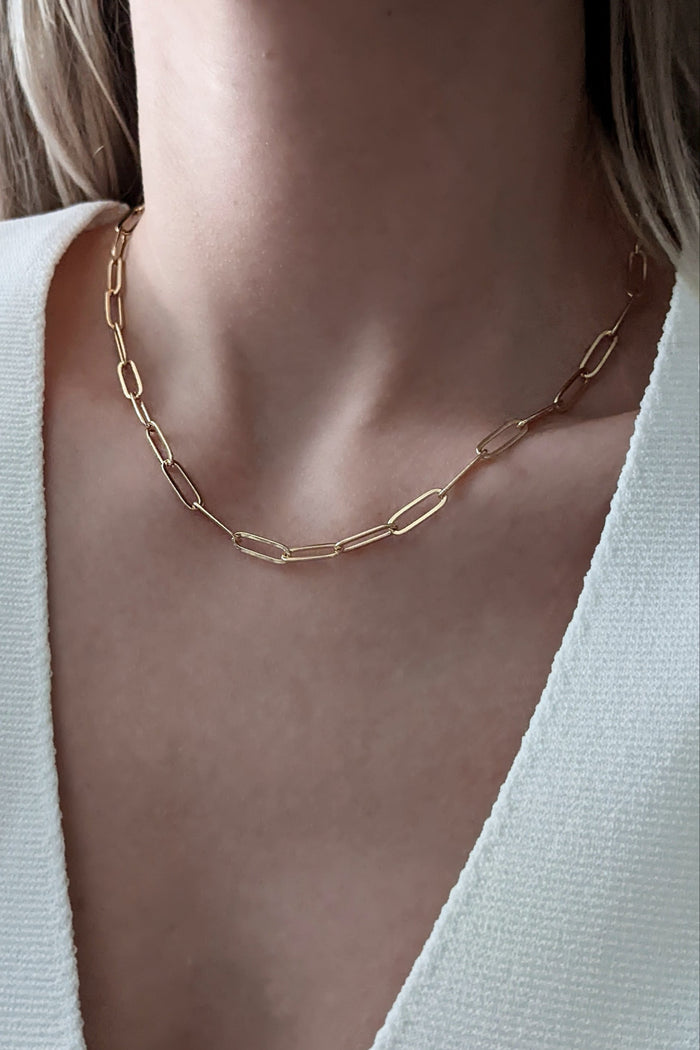 Gold chain necklace worn by a person with a light background