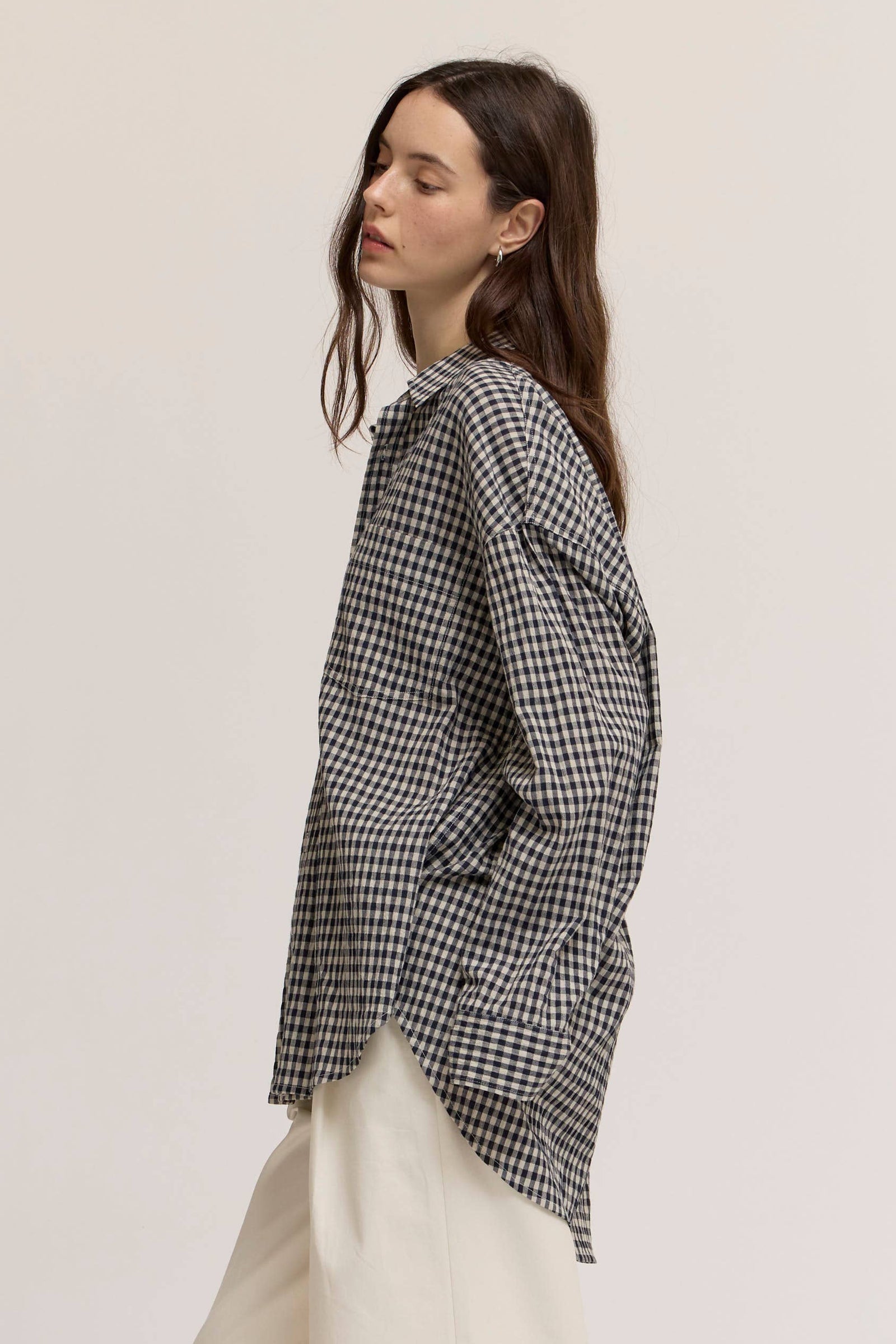 Woman wearing a black and white checkered shirt and white pants on a plain background