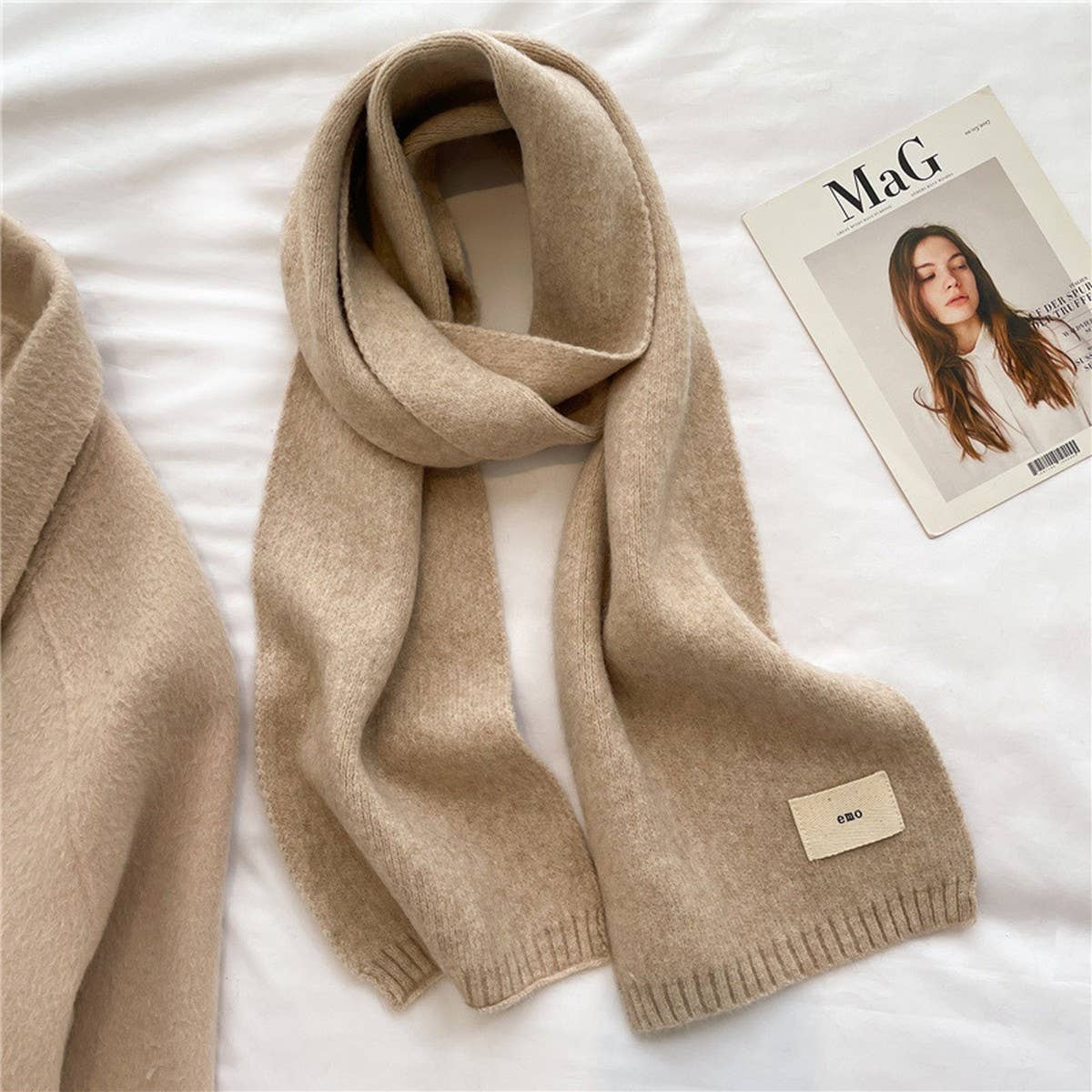 Beige scarf with a brand label on a white surface next to a magazine.