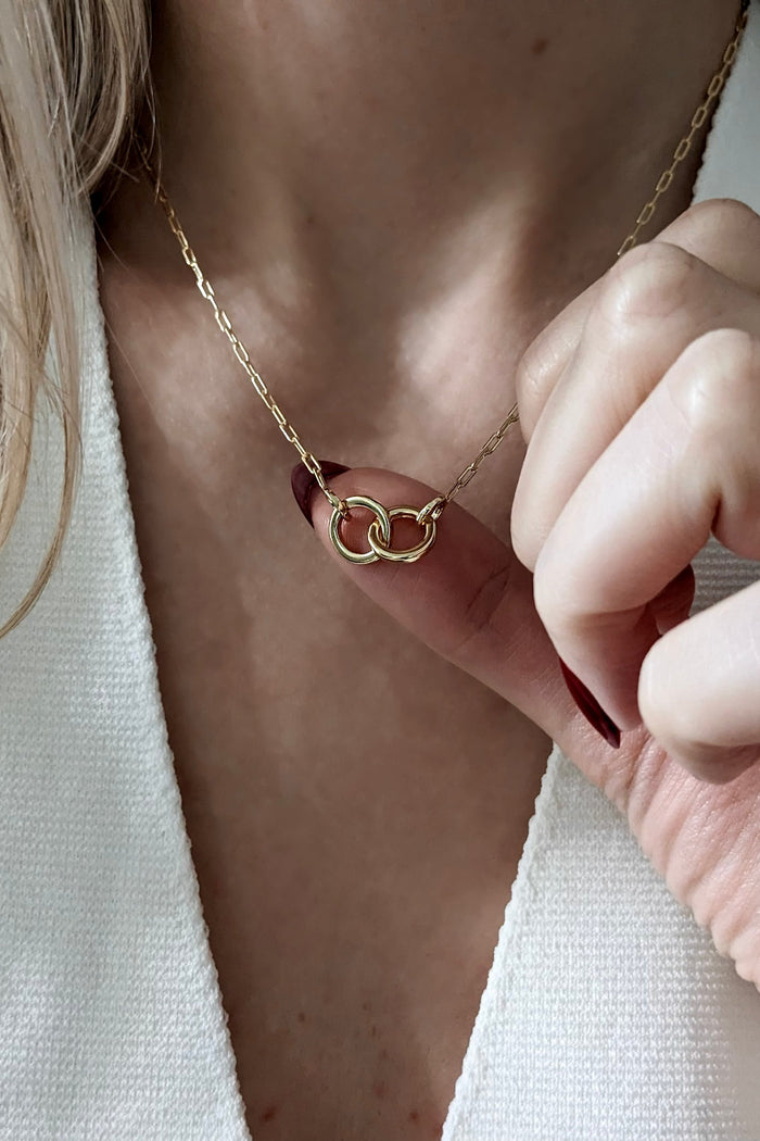 Gold necklace with a unique pendant being adjusted on a person wearing a white top.