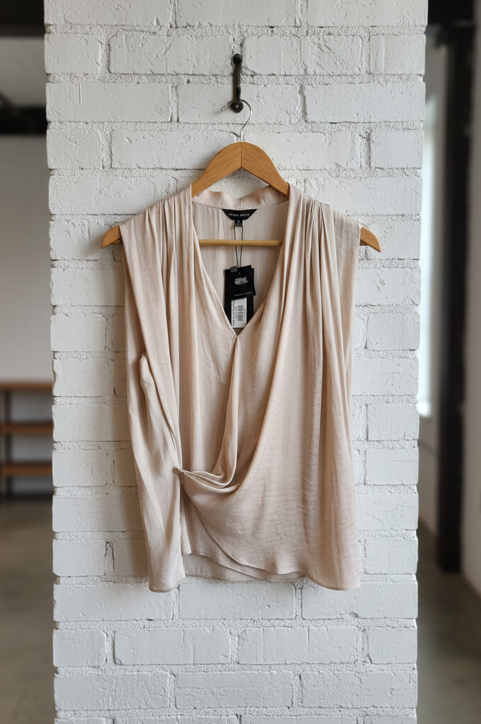 Beige sleeveless top on a wooden hanger against a white brick wall.