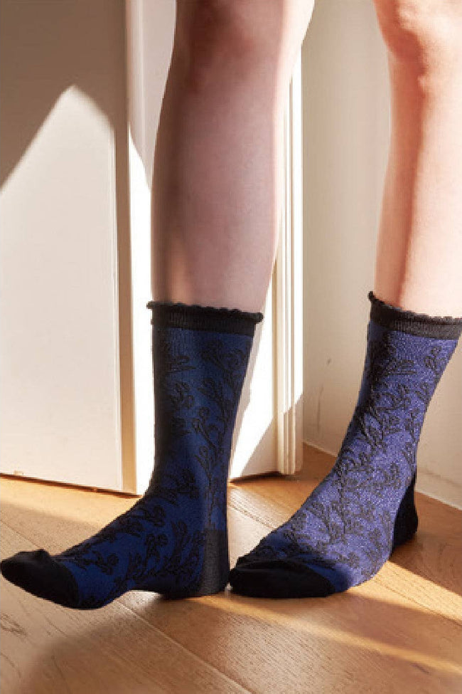 Blue patterned socks worn by a person standing on a wooden floor.