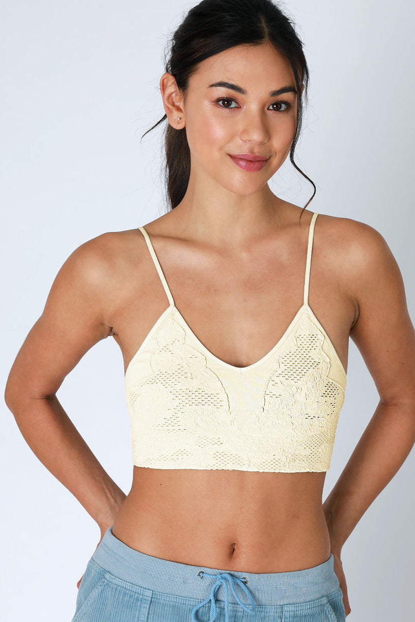 Woman wearing a beige lace bralette with blue pants on a light gray background