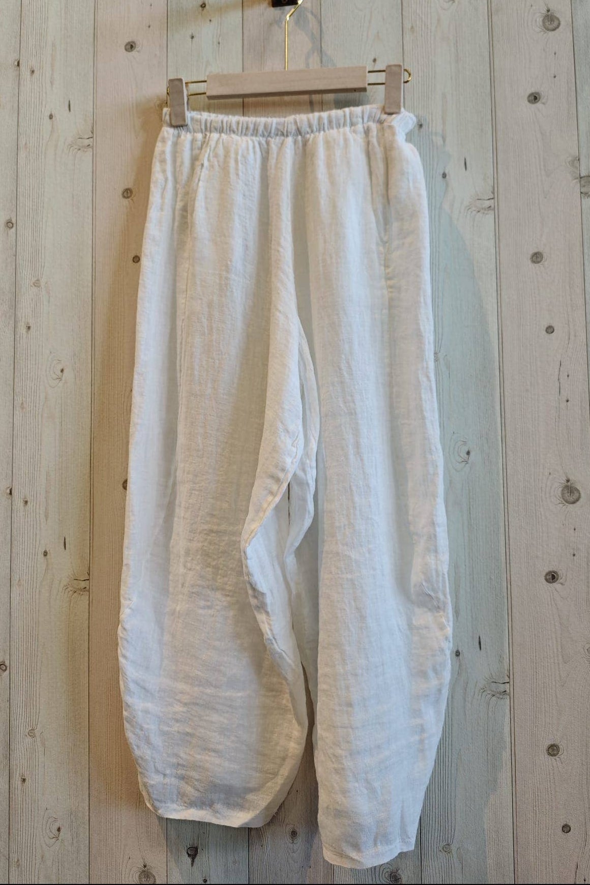 White pants hanging on a wooden hanger against a wooden wall.