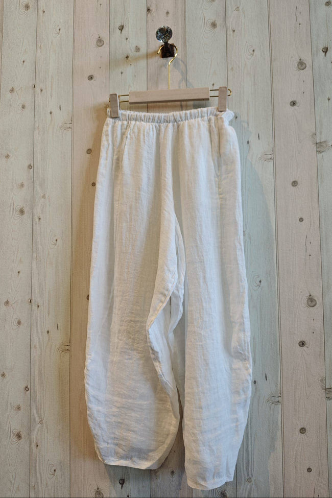 White pants hanging on a wooden hanger against a wooden wall.