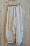 White pants hanging on a wooden hanger against a wooden wall.