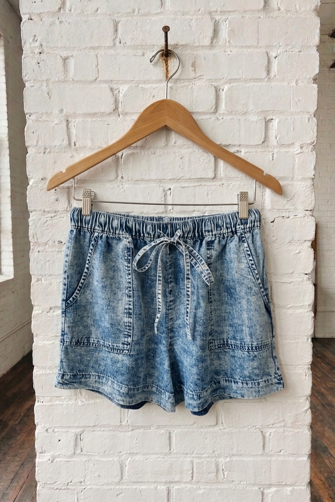 Blue denim shorts on a wooden hanger against a white brick wall.