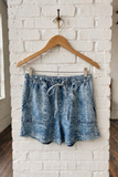 Blue denim shorts on a wooden hanger against a white brick wall.