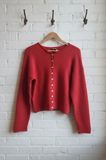 Red sweater on a hanger against a white brick wall