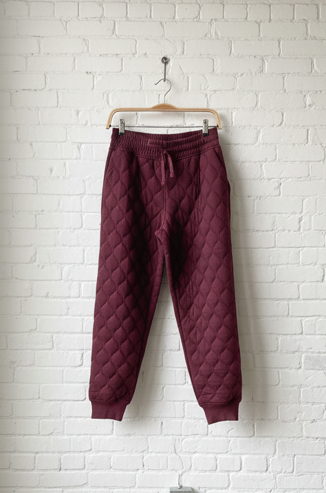 Maroon quilted pants hanging on a hook against a white brick wall.