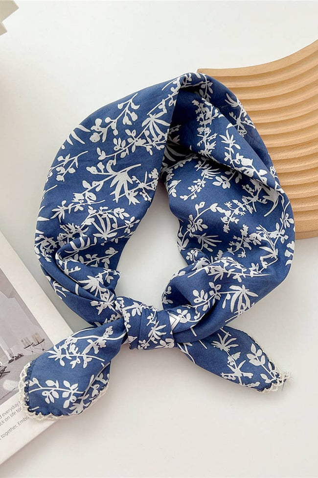 Blue floral patterned scarf on a white surface with a wooden coaster and magazine in the background